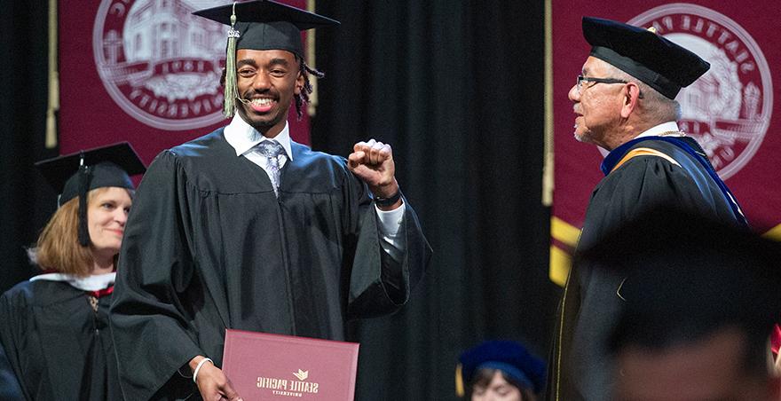 A student in his cap and gown excitedly cheering after receiving his SPU undergraduate diploma at Commencement