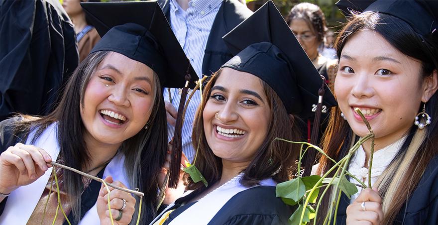 Three female students in their caps and gowns proudly hold their ivy from SPU